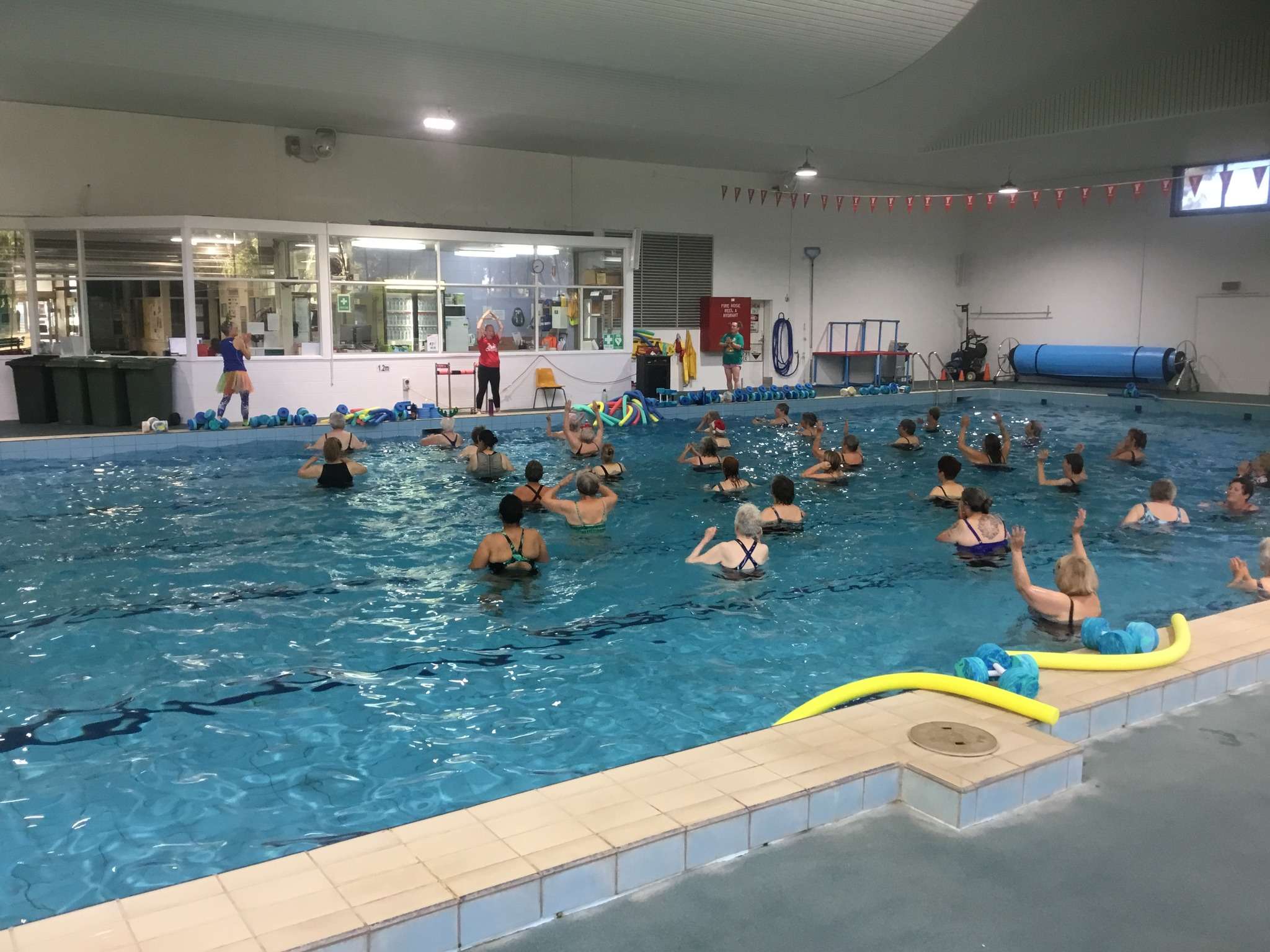 A large group of swimmers doing water aerobics in the large inground indoor pool.