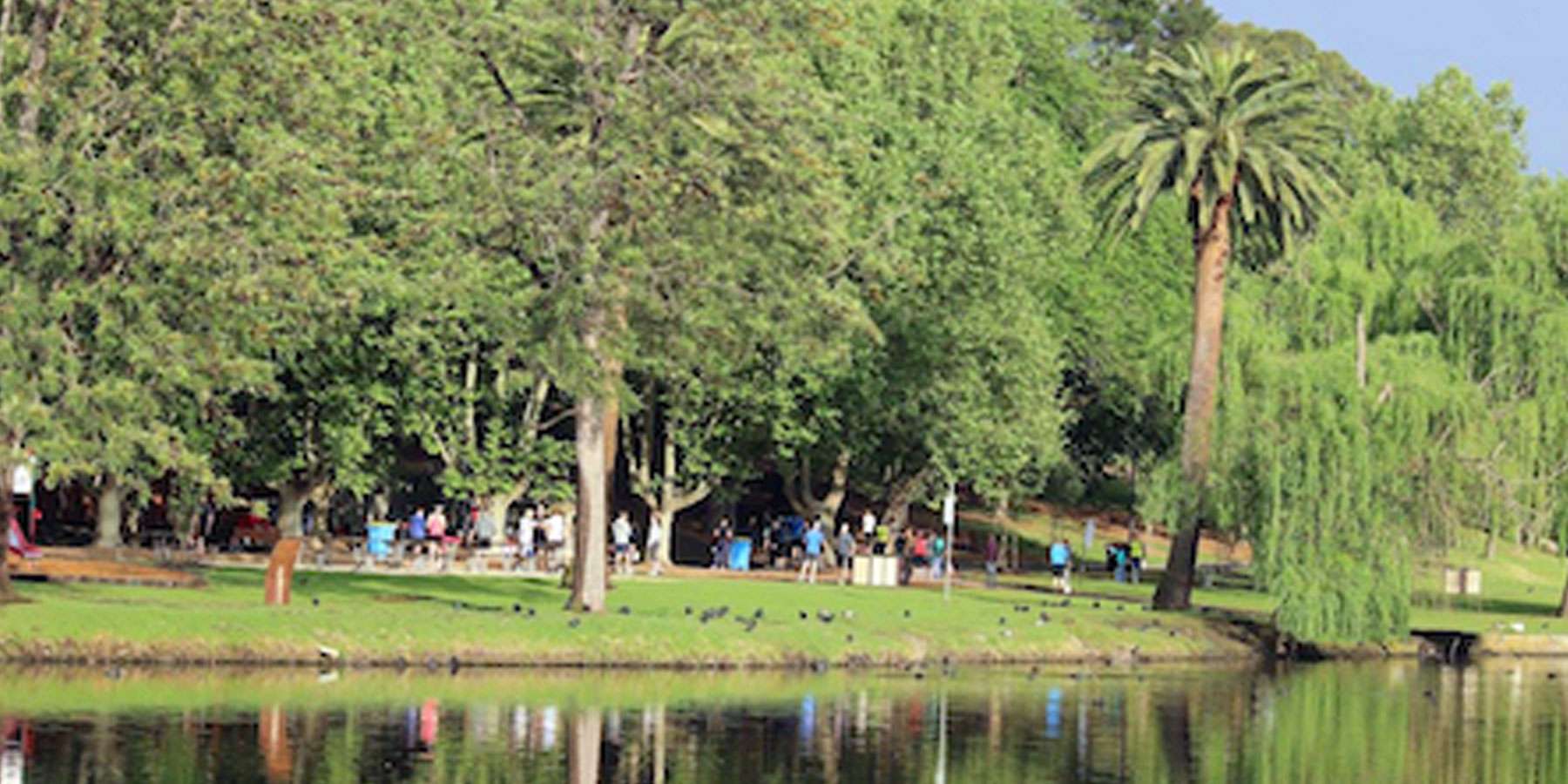 A lake with a backdrop of trees and people running in the distance