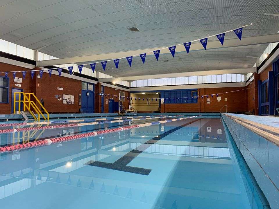 A large inground pool with swimming lanes divided by red ropes and blue flags hanging from the ceiling.
