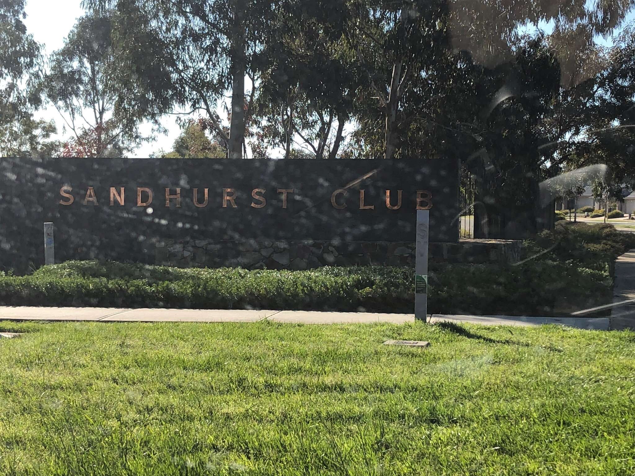 Photo of a grassy area with Sandhurst Club sign in the back ground, surrounded by trees