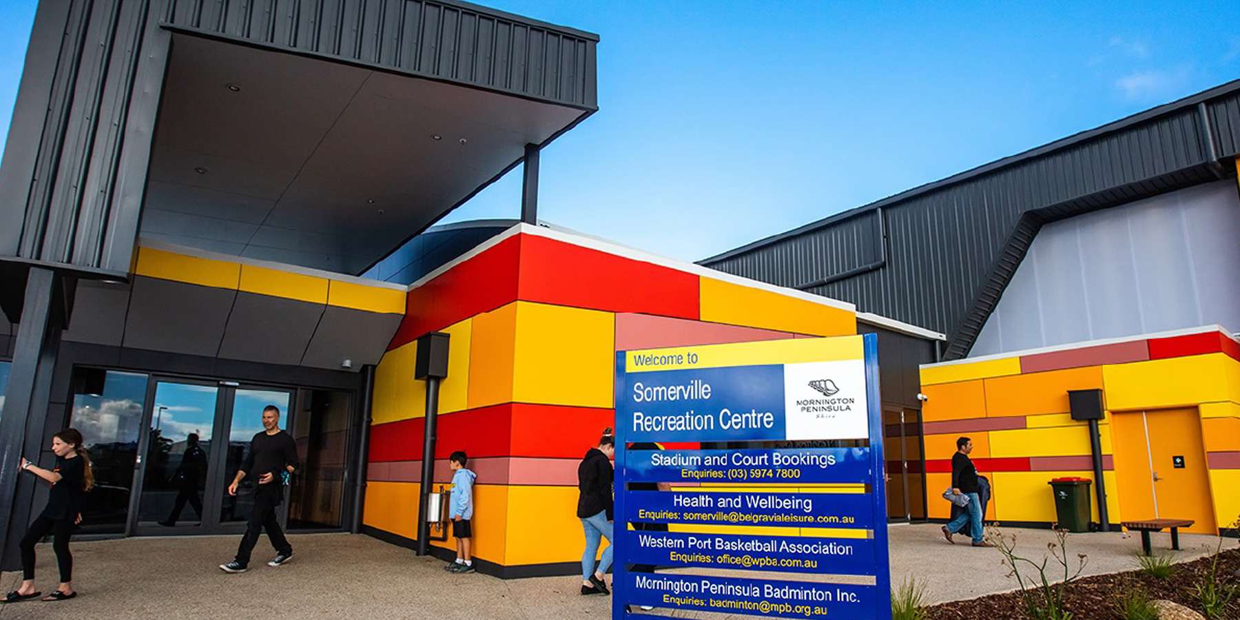 Exterior view of a vibrant, modern building with colorful red and yellow accents, featuring an information sign outside.