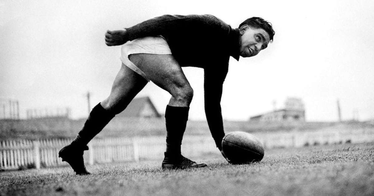 A black and white image of Sir Douglas Nicholls with a football bending down