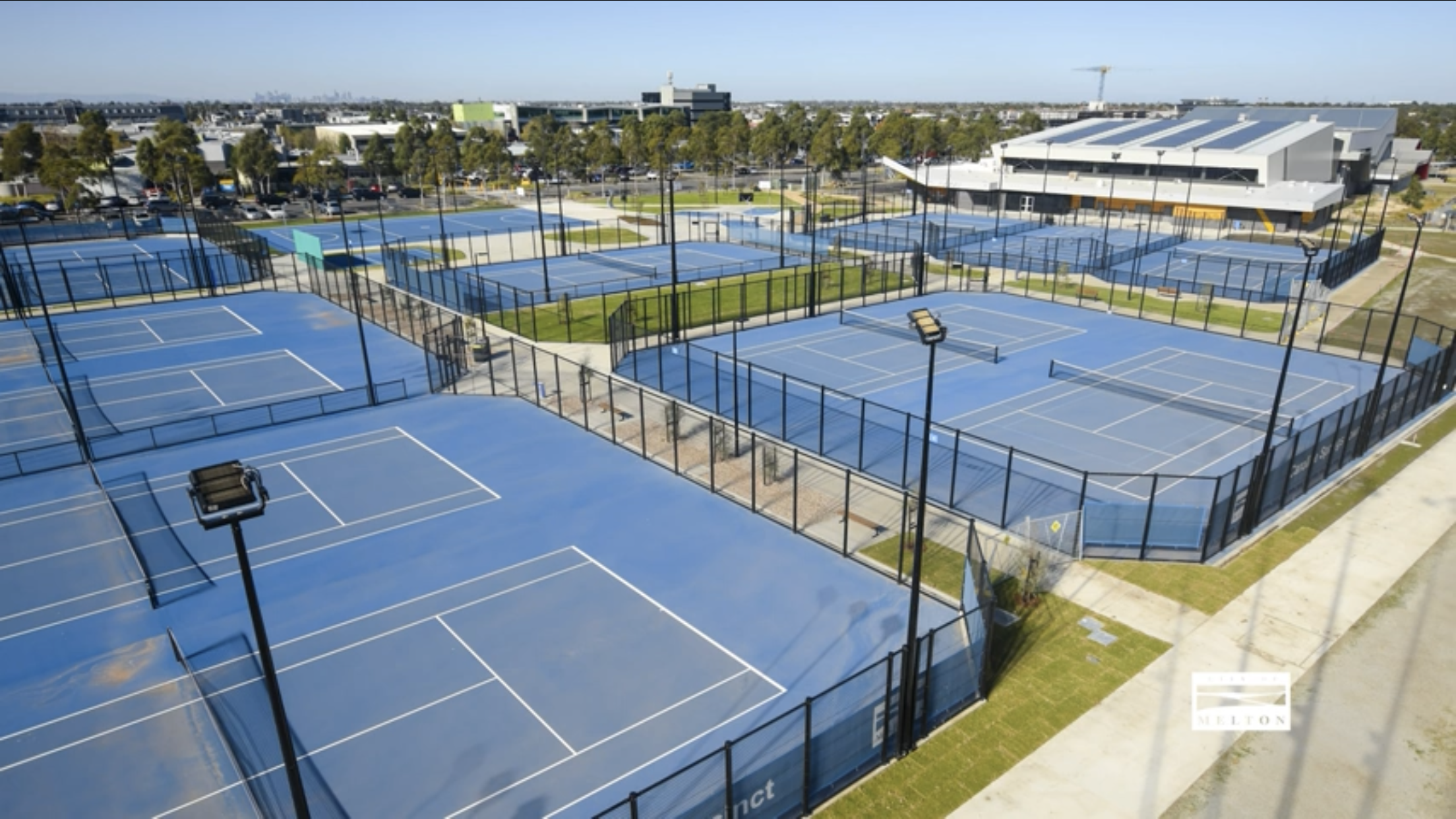 many blue tennis courts with lights and black fencing.