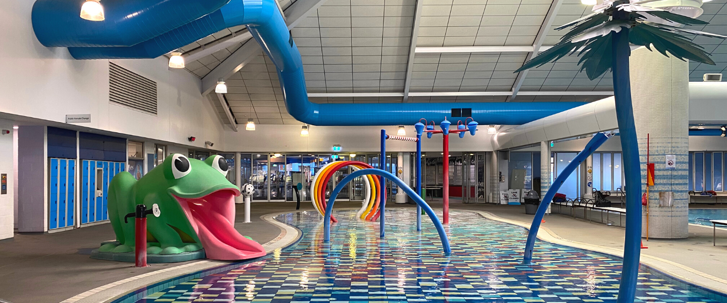 A large inground pool with colourful water features surrounded by grey paved area and